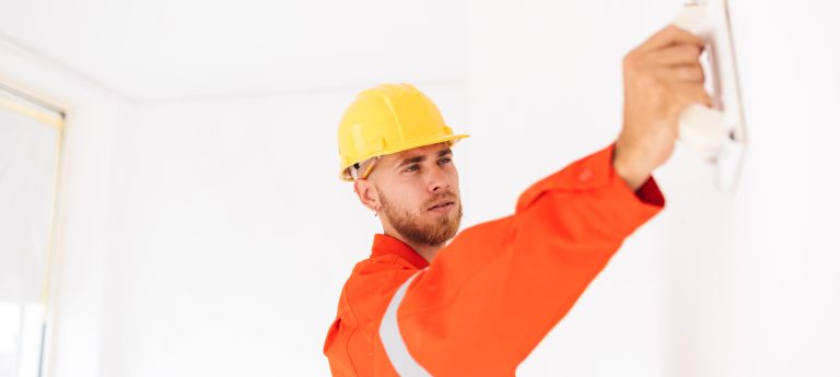 Young Foreman Orange Work Clothes Yellow Hardhat Thoughtfully Using Putty Knife Work Min